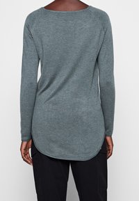 Pitkähihaista puseroa turkoosina, valmistettu pehmeästä neulemateriaalista. Ominaisuuksiin kuuluu leveä kaulus ja kaartuva helma. Minimalistinen ilman lisäkuvioita.