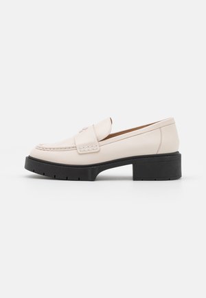 Light beige leather loafers with a stitched front and a textured black platform heel. Features a curved design and a slight elevation.