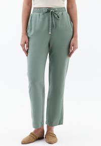 Groene jerseybroek met een relaxte pasvorm, een koord in de taille, zijzakken en rechte pijpen, gecombineerd met geweven instappers.
