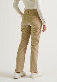 Beige Kordhosen mit schmalem Schnitt, ausgestattet mit Gesäßtaschen und einer weichen Textur, kombiniert mit weißen Sneakers.