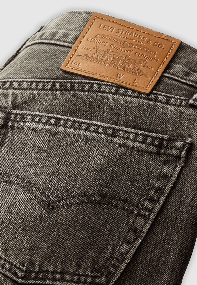 Poche arrière de jean en denim noir avec une étiquette en cuir beige de Levi Strauss & Co. cousue au-dessus de la poche.