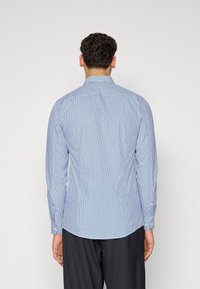 Camisa azul con patrón, de mangas largas, puños de botón y un cuello clásico. Presenta un diseño geométrico sobre un fondo azul claro.