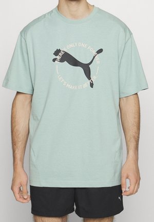 Mężczyzna w jasnozielonej koszulce z dużym czarnym logo Puma i napisem "Jest tylko jedno na zawsze, poprawmy to."