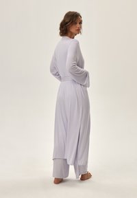 Fioletowy komplet dresowy z długim rękawem, składający się z luźnej bluzki z paskiem w talii oraz spodni, wykonany z miękkiego materiału w swobodnym fasonie.