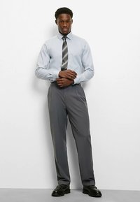 Hellblaues Hemd mit langen Ärmeln, graue Anzughose und schwarze Schuhe. Das Hemd hat einen Button-Down-Kragen und wird mit einer gestreiften Krawatte getragen.