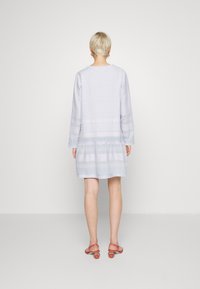 Jasnoniebieska sukienka z długimi rękawami, warstwowym dołem, teksturowanym materiałem i subtelnymi wzorami. Para czerwonych butów ze sprzączkami z tyłu.