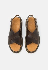 Bruine leren sandalen met gekruiste banden, een tan suède inlegzool en gele stiksels langs de zwarte rubberen zool. Verstelbare gesp aan de zijkant.