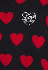 Tissu noir avec des motifs de cœurs rouges et un cœur blanc brodé contenant le texte en cursive « Love Moschino .»