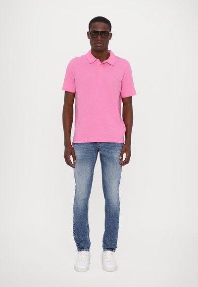 Chemise polo rose en coton, associée à un jean skinny bleu clair. Le modèle porte des lunettes de soleil noires et des baskets blanches.