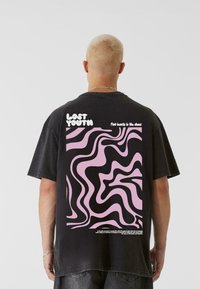 Melnas pārāk lielas T-krekls ar viļņotu rozā un melnu grafiku aizmugurē, virs raksta ir teksts "ZAUDĒTA JAUNĪBA".