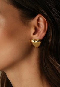 Orecchino a forma di cuore in oro con superficie liscia e riflettente, caratterizzato da una finitura lucida e bordi arrotondati. Il design mette in evidenza una forma tridimensionale.