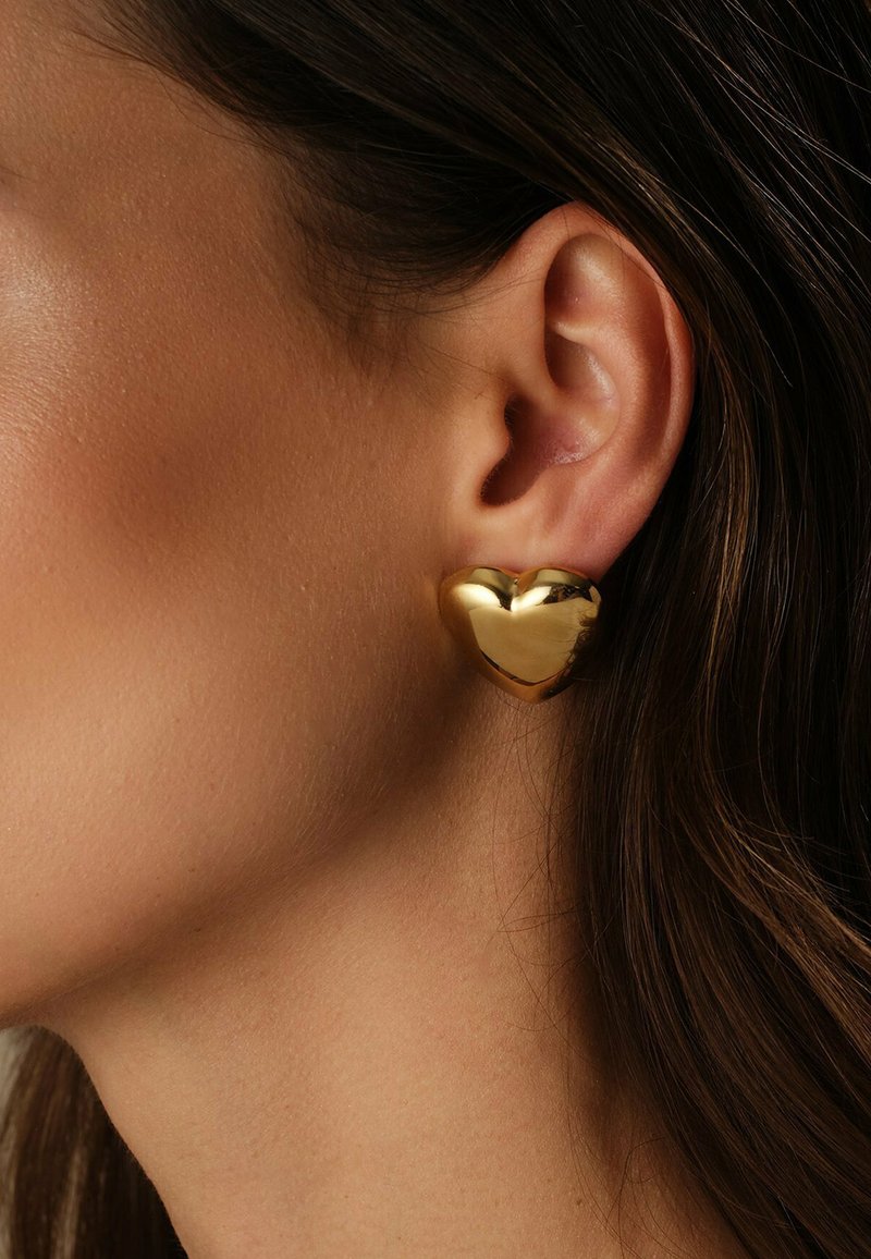Orecchino a forma di cuore in oro con superficie liscia e riflettente, caratterizzato da una finitura lucida e bordi arrotondati. Il design mette in evidenza una forma tridimensionale.