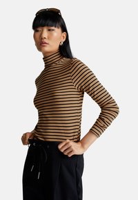 Gestreifter Rollkragenpullover in Beige und Schwarz, mit langen Ärmeln und figurbetontem Design. Das Material wirkt glatt und dehnbar.