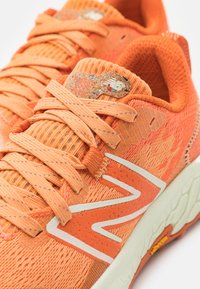 Scarpe atletiche arancioni con tomaia in rete testurizzata, lacci e logo bianco. Presentano un accento in sughero sulla linguetta e una suola ammortizzata.