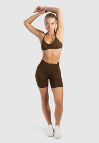 Conjunto atlético marrón que incluye un bralette con detalle fruncido y shorts de cintura alta. Textura suave, diseño ajustado y sin logotipos visibles.