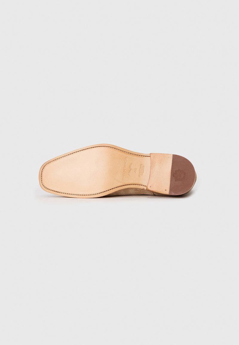 Semelle de chaussure en cuir, beige, avec une texture lisse et une forme arrondie. Présente un talon en caoutchouc marron et des coutures visibles le long du bord.