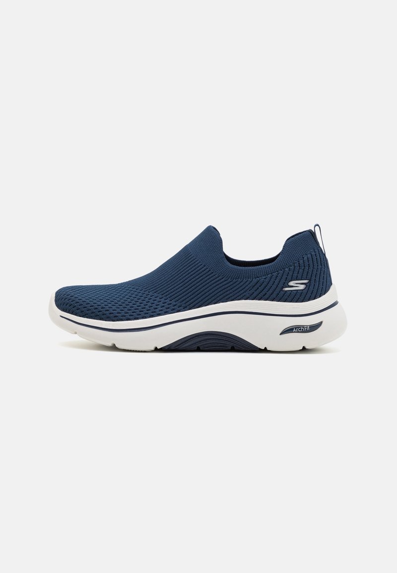Chaussure de sport slip-on bleu marine avec semelle blanche, dessus en maille texturée et logo sur le côté, conçue pour le confort et le soutien de la voûte plantaire.