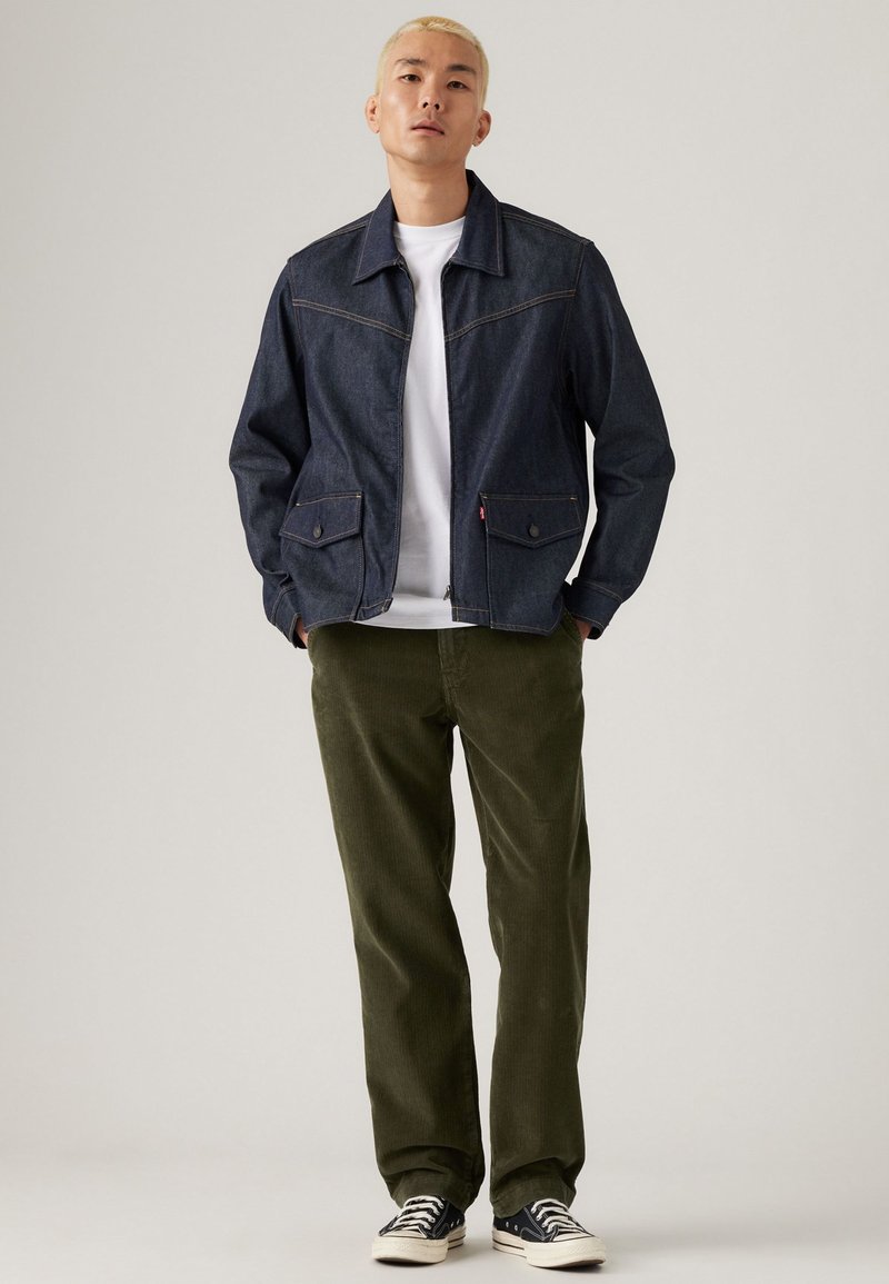Dark denim jacket with two front pockets, white shirt underneath, olive corduroy pants, and black sneakers with white soles.