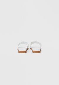Hvite flip-flop sandaler med glatt plastoverdel og brun gummisåle, med et minimalistisk design og åpen bak.