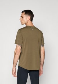 T-shirt verde-azeitona de manga curta com decote redondo e detalhe do logótipo nas costas. O tecido parece suave e leve.