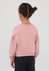 Felpa rosa con collo rotondo, polsini e orlo a costine. Vestibilità ampia con spalle drop. Texture morbida, indossata sopra pantaloni scuri.