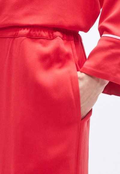 Κόκκινο ένδυμα με υφή, διαθέτει ελαστική μέση και πλαϊνές τσέπες. Το μανίκι έχει αντίθετη λευκή λεπτομέρεια.