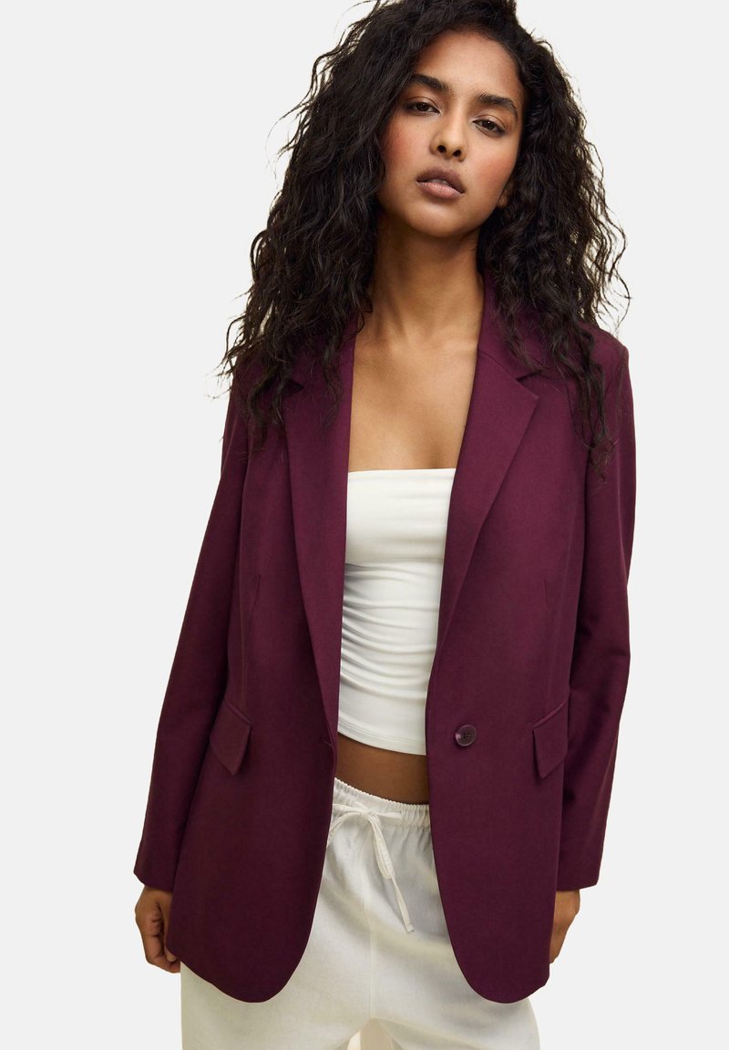 Burgundské sako se střihem na míru, s dvěma předními kapsami a zapínáním na jeden knoflík, nošené přes bílé crop top.