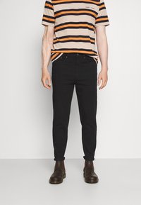 Maglietta a righe nei colori arancione, nero e beige, abbinata a jeans neri e stivali alla caviglia marroni, tutto visibile dalla vita in giù.