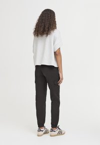 Šedá zkrácená mikina, černé cargo kalhoty s elastickými manžetami a vícolorsné tenisky. Texturované látky, volný střih, minimalistický design.