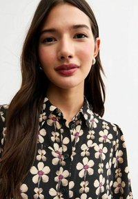 Floral button-up shirt with a black background, featuring cream-colored flowers with pink centers. Smooth fabric texture.