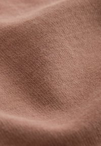 Detailní záběr světle hnědého pleteného materiálu ukazující jemnou texturu a jemné švy na mírně zakřiveném povrchu.