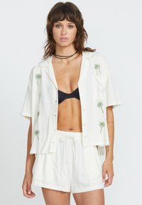 Chemise blanche à manches courtes avec broderie de palmiers verts, boutonnée sur le devant, et une poche poitrine, assortie à un short blanc à cordon de serrage.