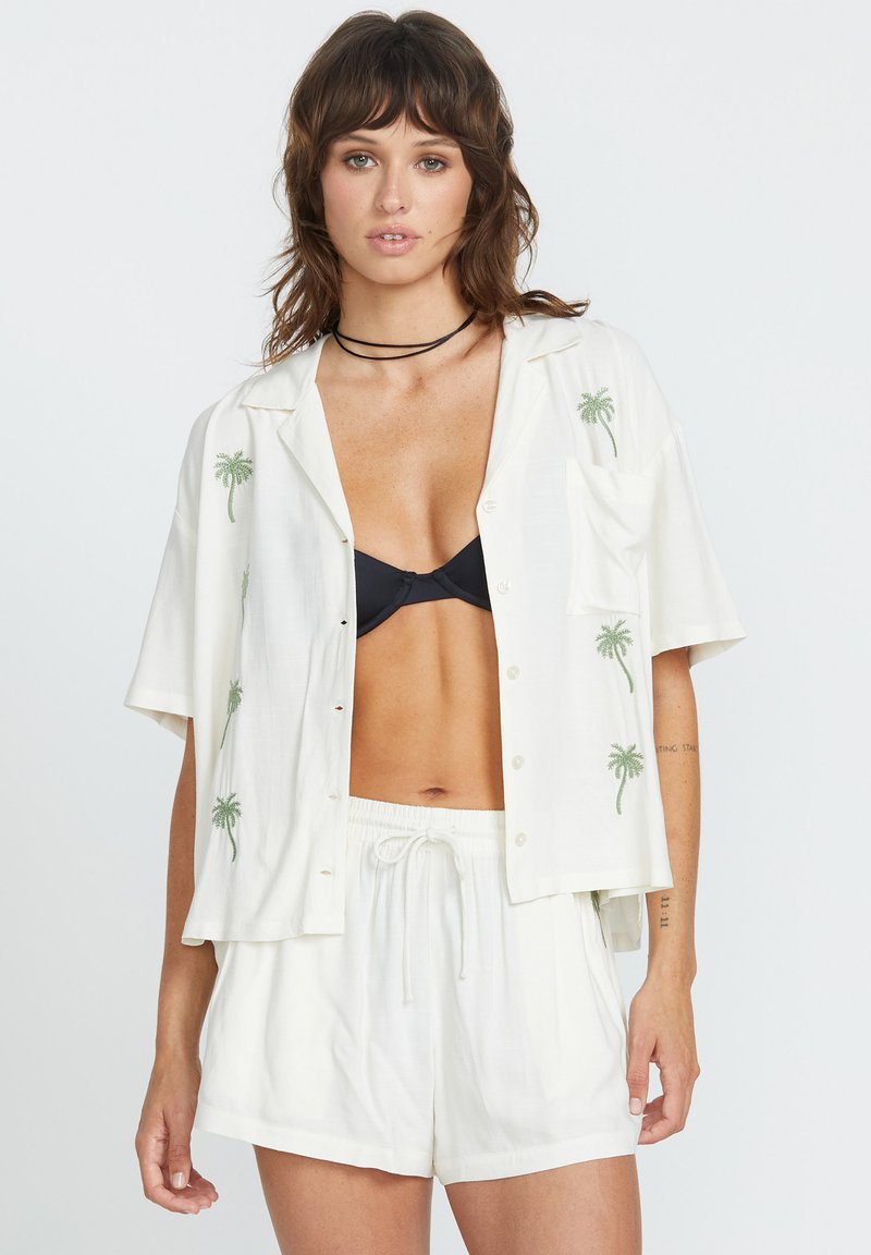 Chemise blanche à manches courtes avec broderie de palmiers verts, boutonnée sur le devant, et une poche poitrine, assortie à un short blanc à cordon de serrage.