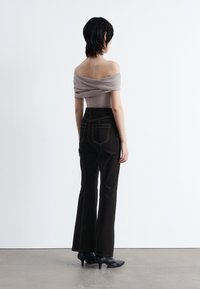 Beige Oberteil mit schulterfreiem Schnitt und drapierten Details, kombiniert mit schwarz hochtaillierten Schlagjeans, die kontrastierende Nähte und Gesäßtaschen haben.