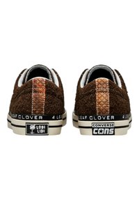 Brown suede sneakers with a textured back panel, white accents, and black rubber soles. Branding "Lobi Libi" and "Converse" visible on heels.