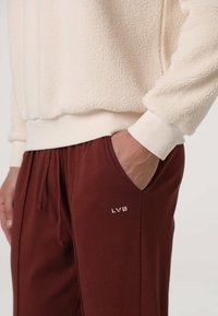 Felpa crema in pile con polsini a coste, abbinata a pantaloni della tuta bordeaux con vita a coulisse e logo "LVB" bianco.