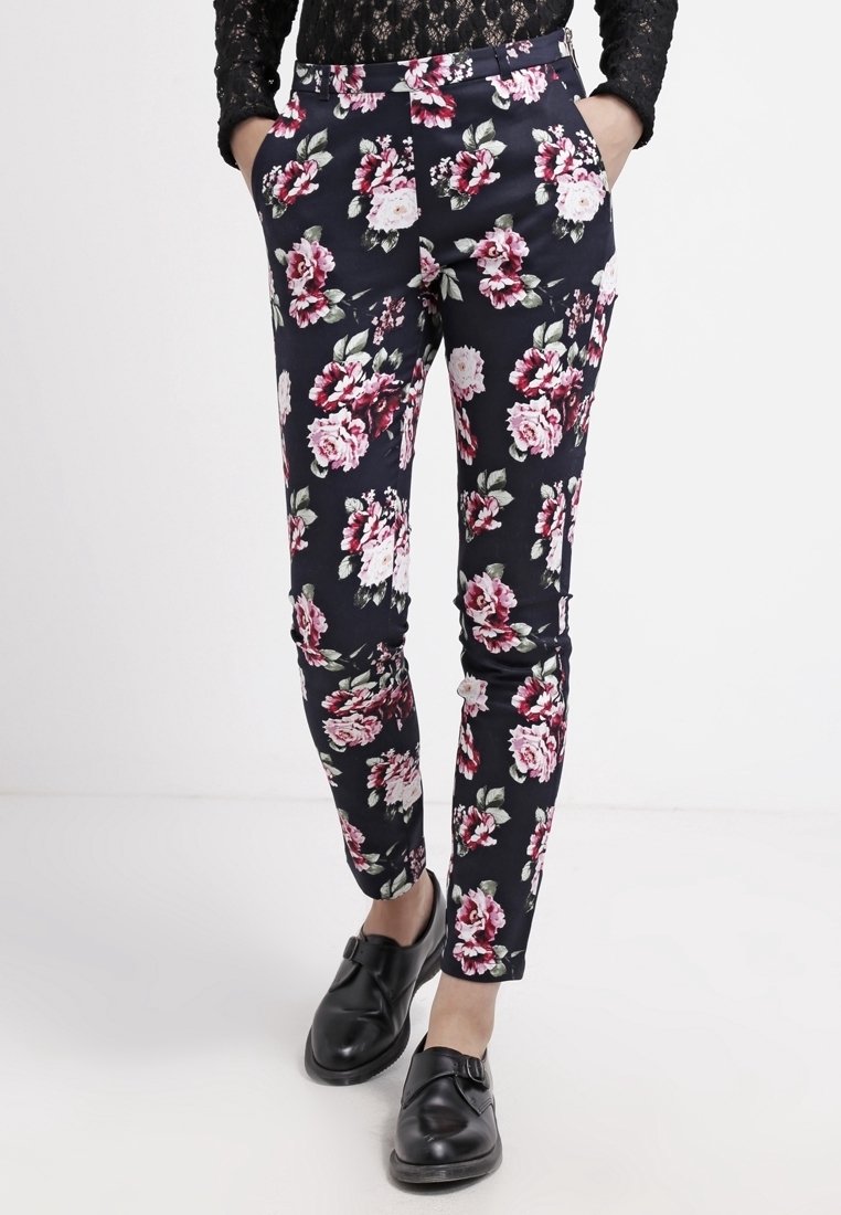 Květinové kalhoty černé barvy se vyznačují živým vzorem růžových a bílých květin. Úzký střih s bočními kapsami a zdobením pasu.