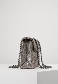 Bolso de mano metálico de forma estructurada, con cadena y parte superior plegada, que exhibe una superficie texturizada en gris plateado.