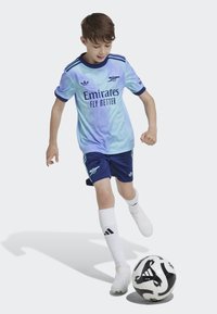 Maillot de football dégradé bleu et aqua avec des accents marine, logo "Emirates Fly Better", associé à un short marine et des chaussettes blanches. Ballon de football noir et blanc.