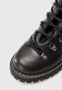 Bota de caminhada em couro preto com sola grossa, ilhós de metal e atacadores pretos sobre um fundo branco.