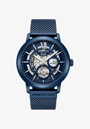 Sininen Kenneth Cole automaattirannekello verkkomaisella rannekkeella, skelettonäyttö paljastaa sisäiset vaihteet, ja hopeiset roomalaiset numerot XII yläosassa.