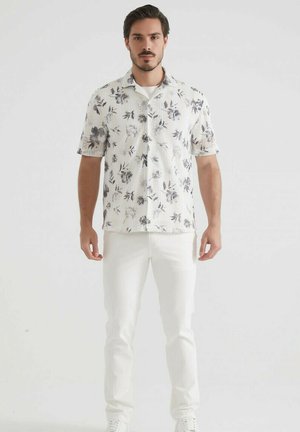 Chemise à manches courtes blanche à motifs floraux avec des accents gris, dotée d'une fermeture à boutons et d'une coupe décontractée, assortie à un pantalon blanc et des baskets.
