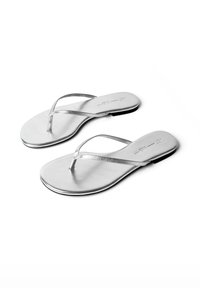 Paire de sandales plates argentées à lanières fines et semelles noires sur fond blanc.