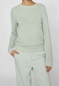 Pull vert clair en maille avec un motif texturé, encolure ronde et manches longues. Comprend des poignets et un ourlet côtelés. Assorti à un pantalon coordonné.
