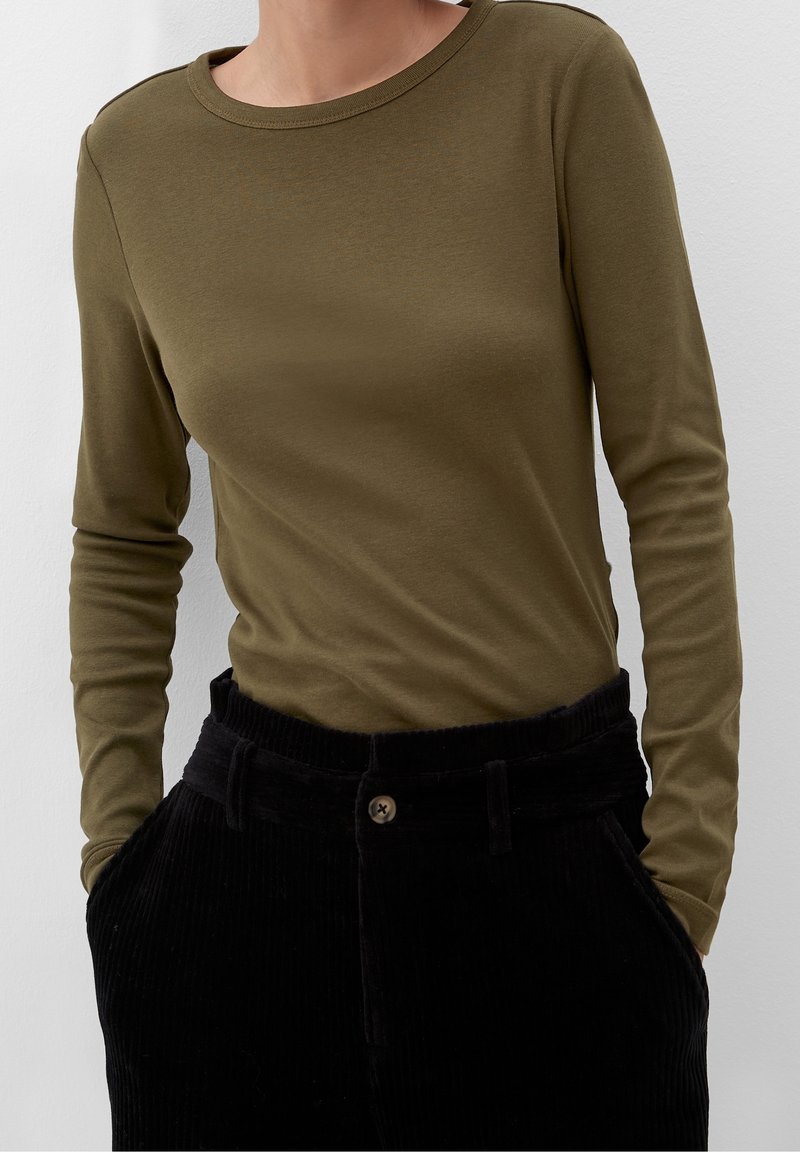 Maglia a maniche lunghe verde oliva con scollatura tonda, abbinata a pantaloni neri in corduroy a vita alta con chiusura a bottone e tasche laterali.