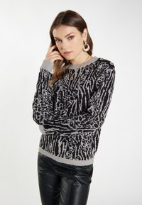 Zwart en grijs gebreid sweater met een patroon, lange mouwen, geribbelde halslijn en manchetten, voorzien van decoratieve schouderknopen. Gepaard met zwarte broeken.