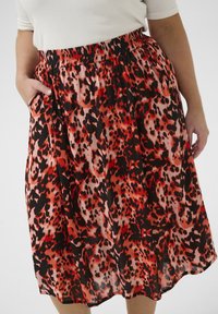 Jupe plissée dans un imprimé léopard rouge vif et noir, avec une taille élastique et des poches latérales. Fabriquée en tissu léger.