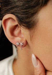 Orecchini di forma floreale argentati con pendenti, caratterizzati da gemme trasparenti. Il design include dettagli testurizzati e una finitura lucida.