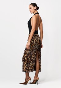 Czarny body z odkrytymi ramionami i głębokim dekoltem na plecach, w połączeniu ze spódnicą w panterkę z bocznymi rozcięciami, uzupełnione brązowymi, szpiczastymi szpilkami.