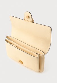 Bežová textúrovaná kožená kabelka so zlatým uzáverom otvorená tak, aby ukázala dva hlavné priehradky na bielom pozadí.